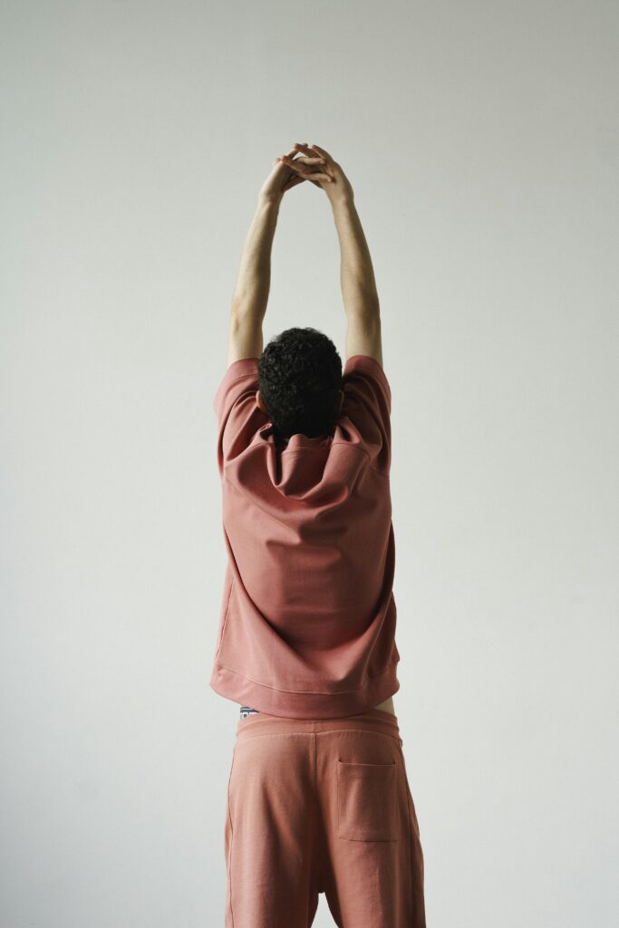 Rear view of a person stretching upwards in a pink outfit against a plain background.